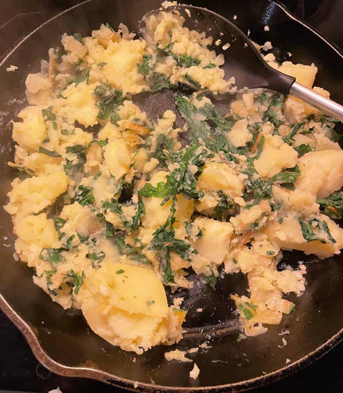 stirring potatoes and chard in a black skillet.