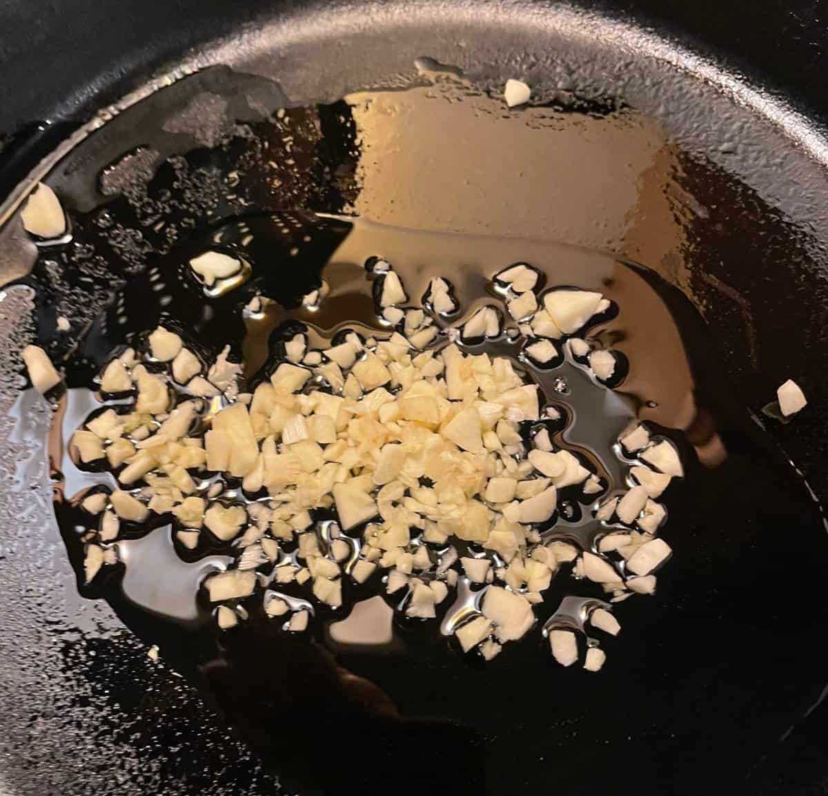 sautéing minced garlic in a black skillet with olive oil.