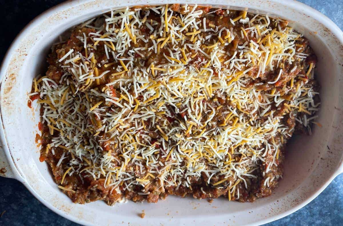 Hatch chile enchiladas in a white baking dish with cheese sprinkled over the top.