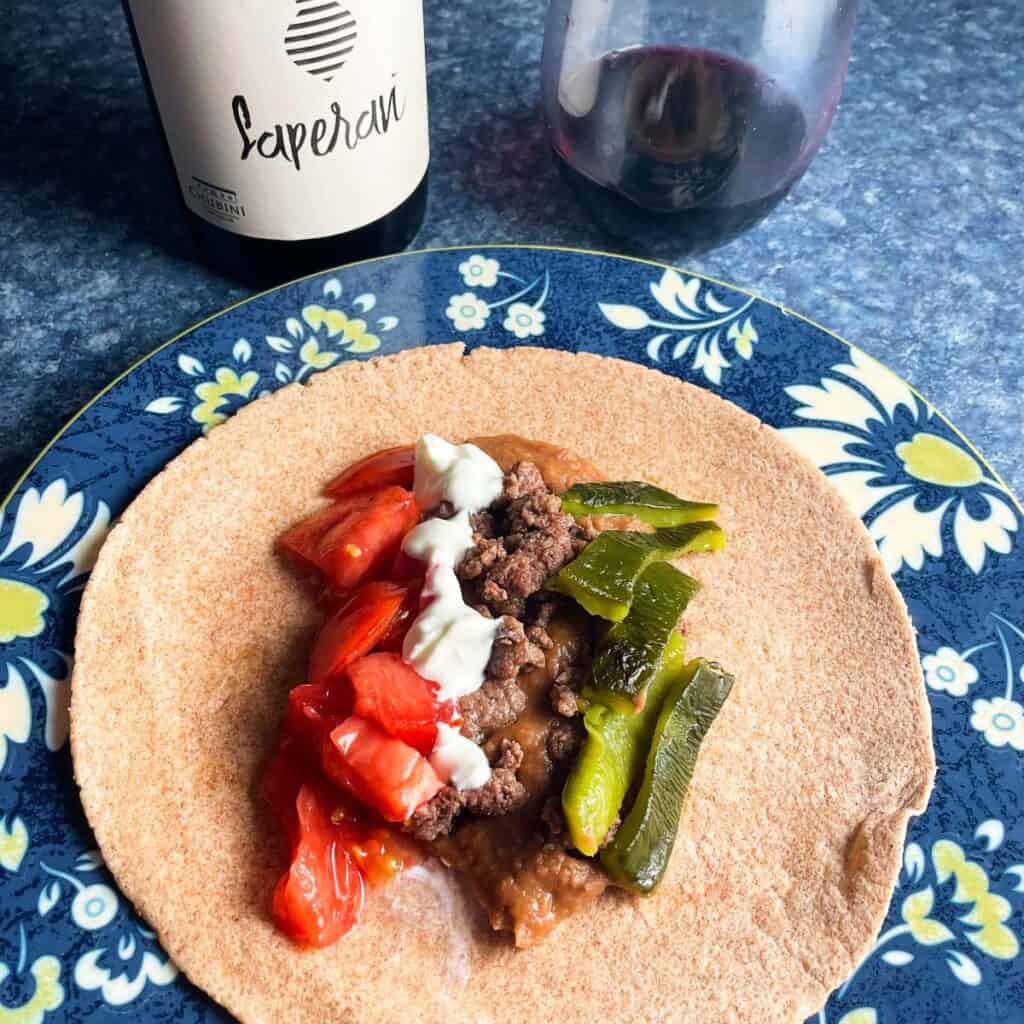 beef and bean tacos with peppers and tomatoes, served with a red wine.