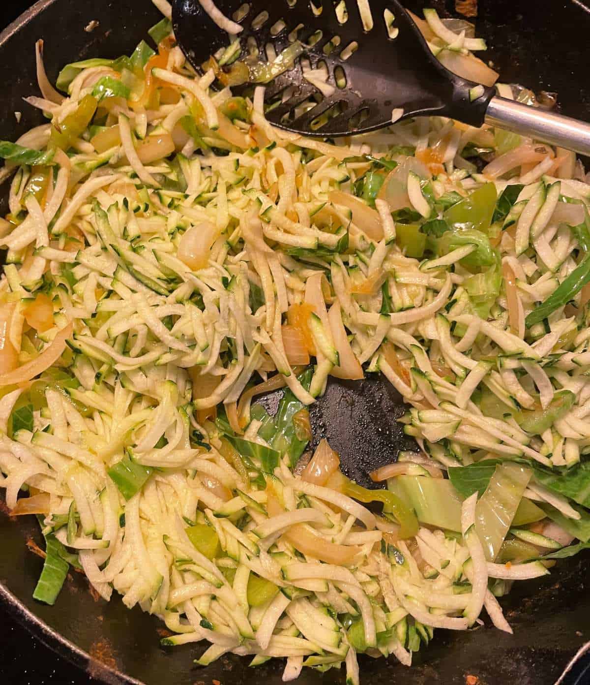 shredded zucchini and cabbage being sautéed in a skillet with onions.