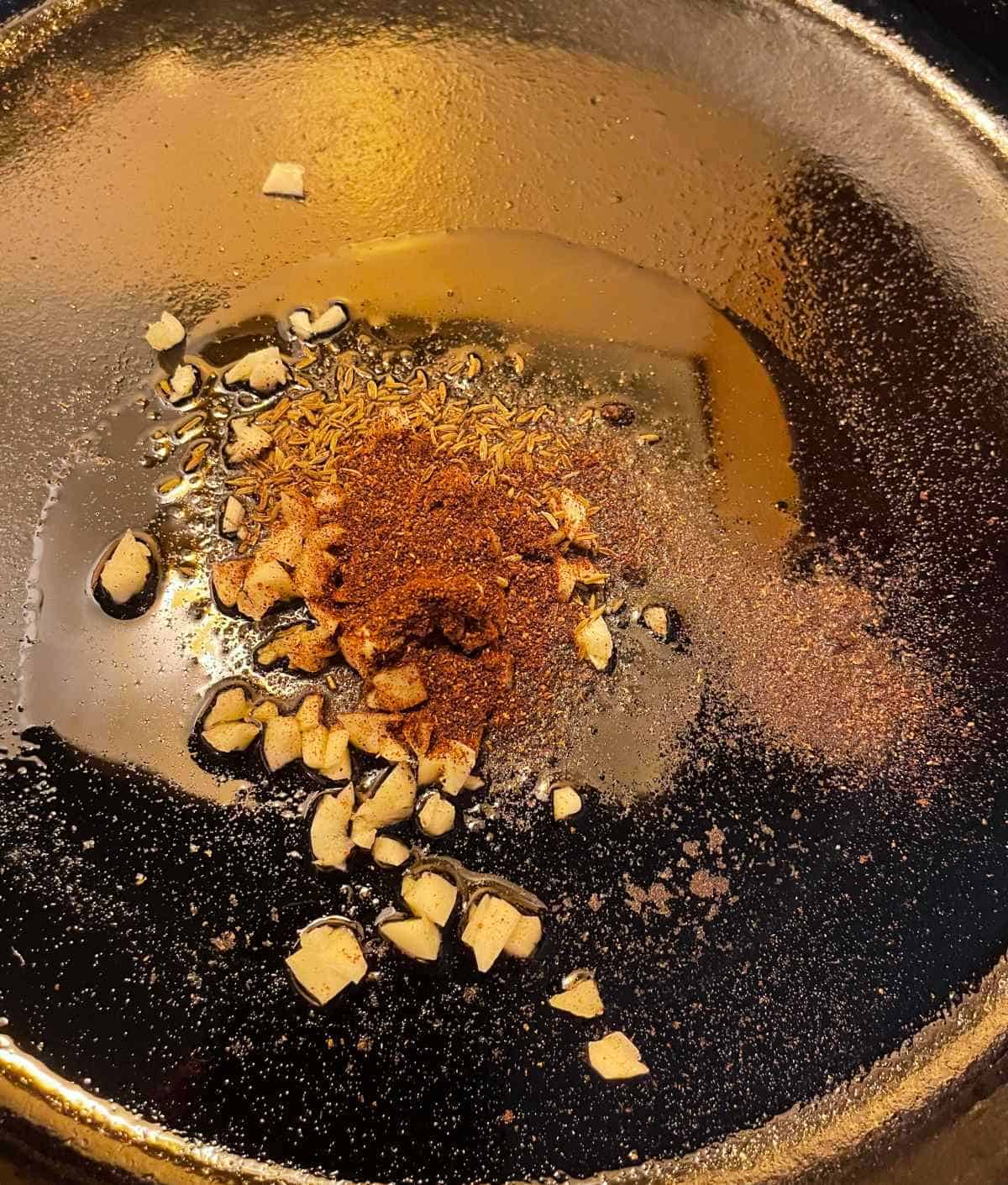 garlic and spices heating in a black skillet.