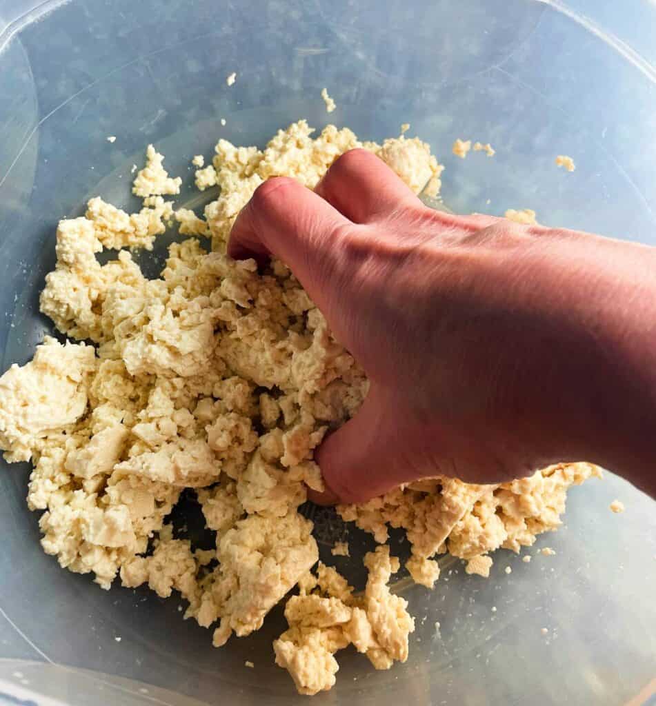 tofu in a bowl being broken into pieces by someone's right hand.
