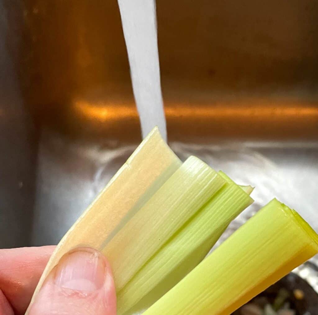 peeling back layers of a leek to clean it under running water.