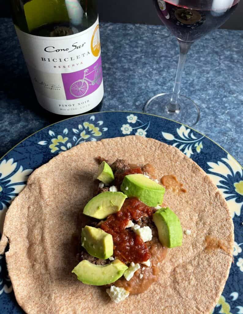beans and ground beef on a whole wheat soft taco, topped with salsa and avocado. Served with a red wine.