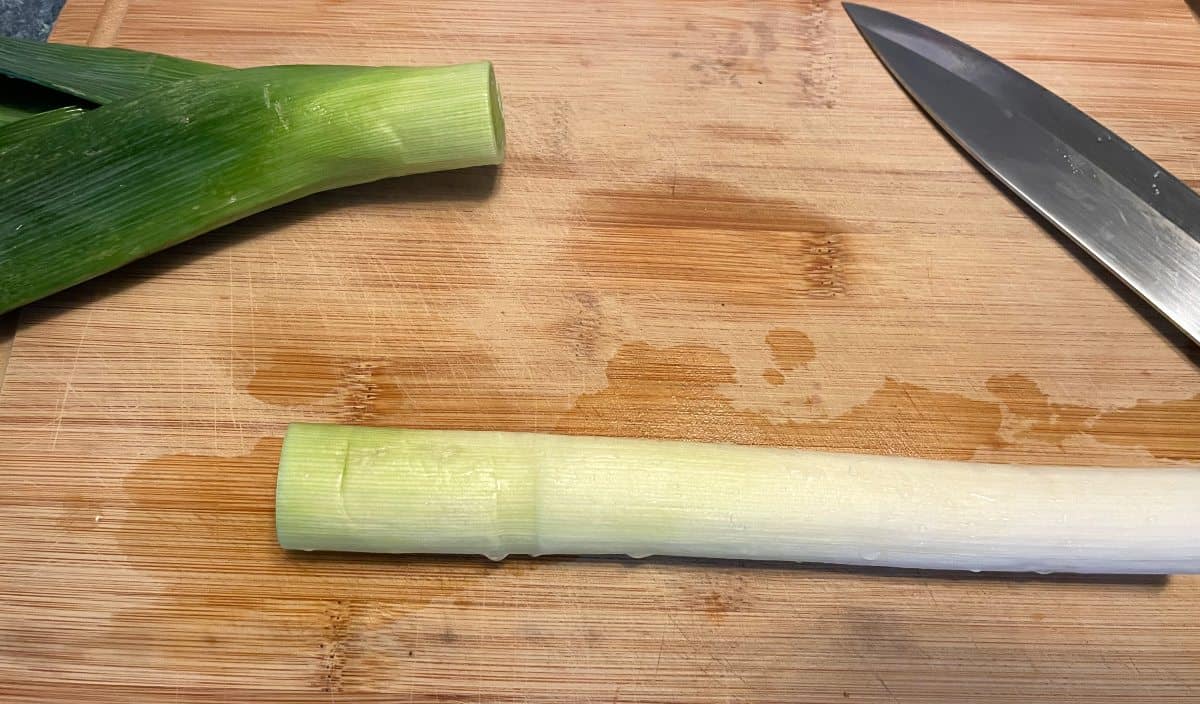 a dark green leek top and white leek bottom, on a cutting board after being cut into two sections.