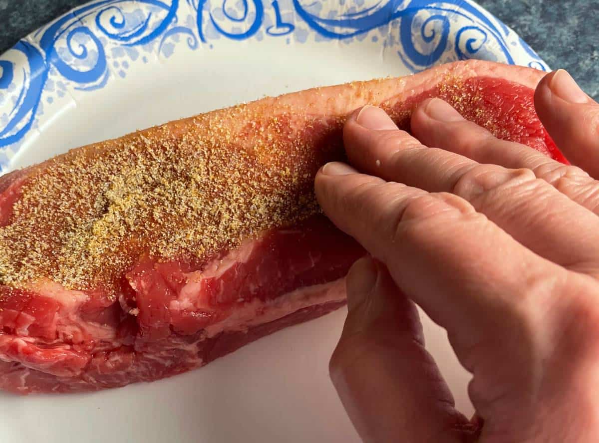 fingers rubbing spices into NY strip steak.