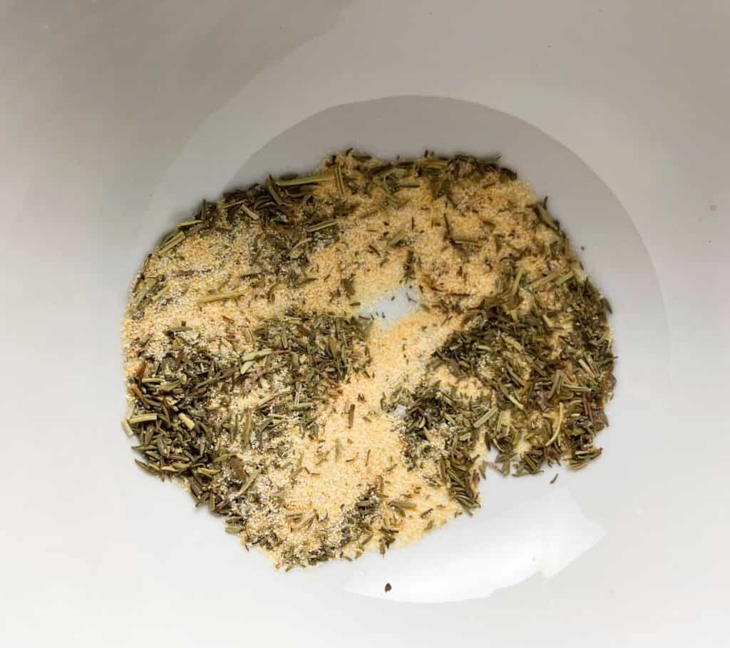 garlic powder, salt, dried thyme and rosemary combined in a white bowl to make a spice rub.