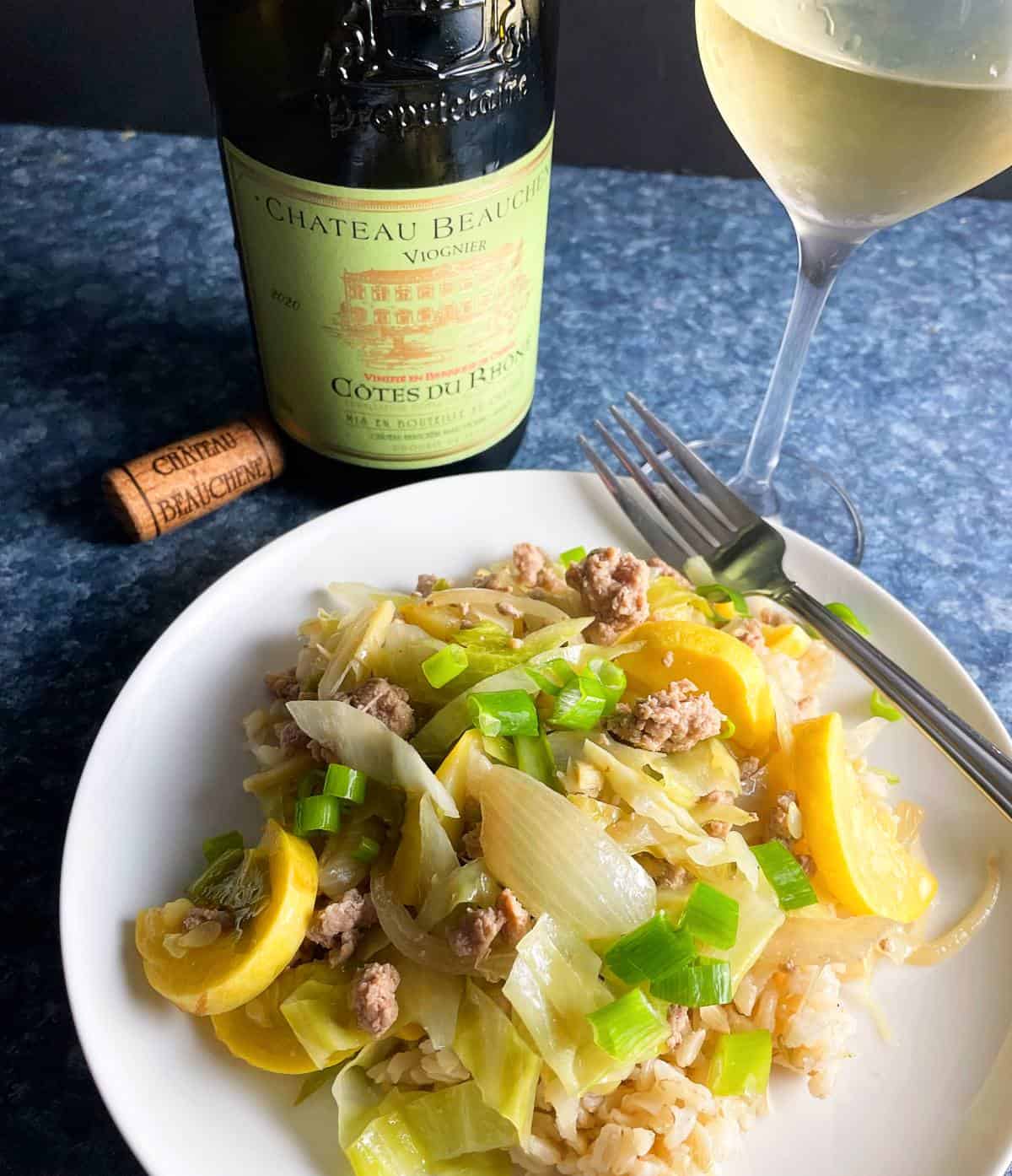 ground pork stir fry with summer squash, served on a white plate, along with a Viogner white wine.