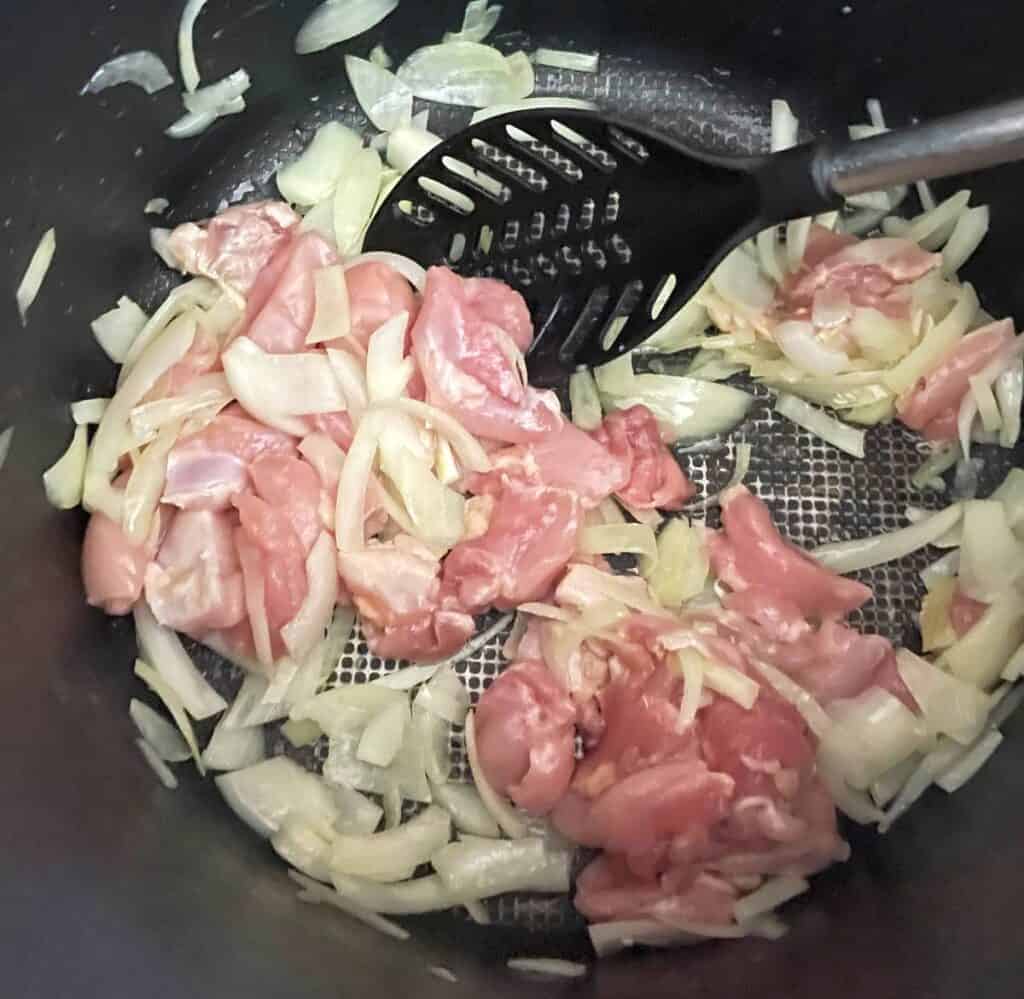 adding raw chicken to a black pot with onions in it.
