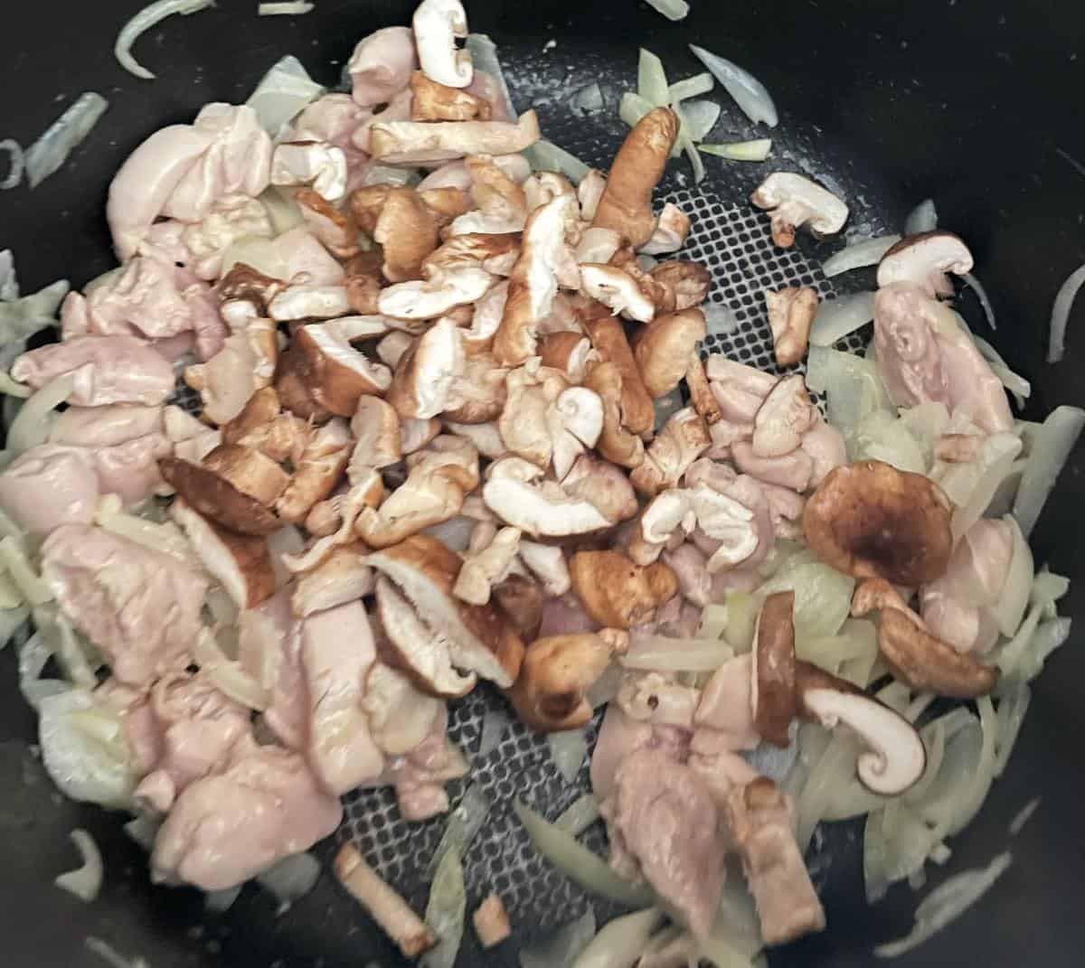 shiitake mushrooms added to a pan with chicken and onions.