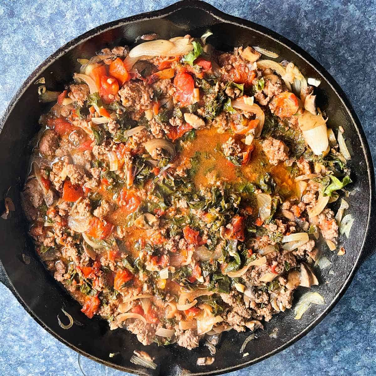 ground beef and kale along with tomatoes in a large black skillet.