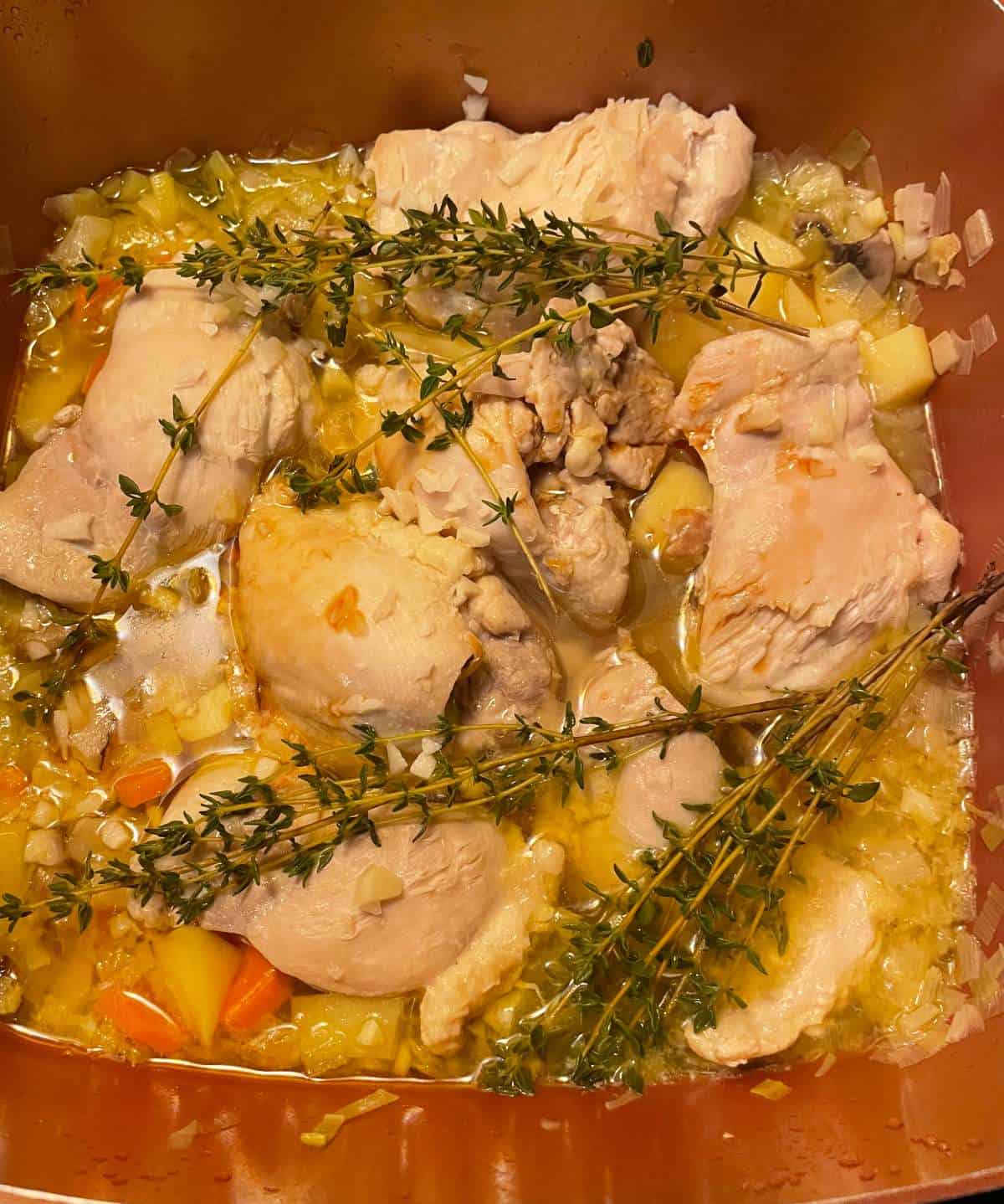 chicken thighs in a pan with vegetables, topped with fresh thyme sprigs.