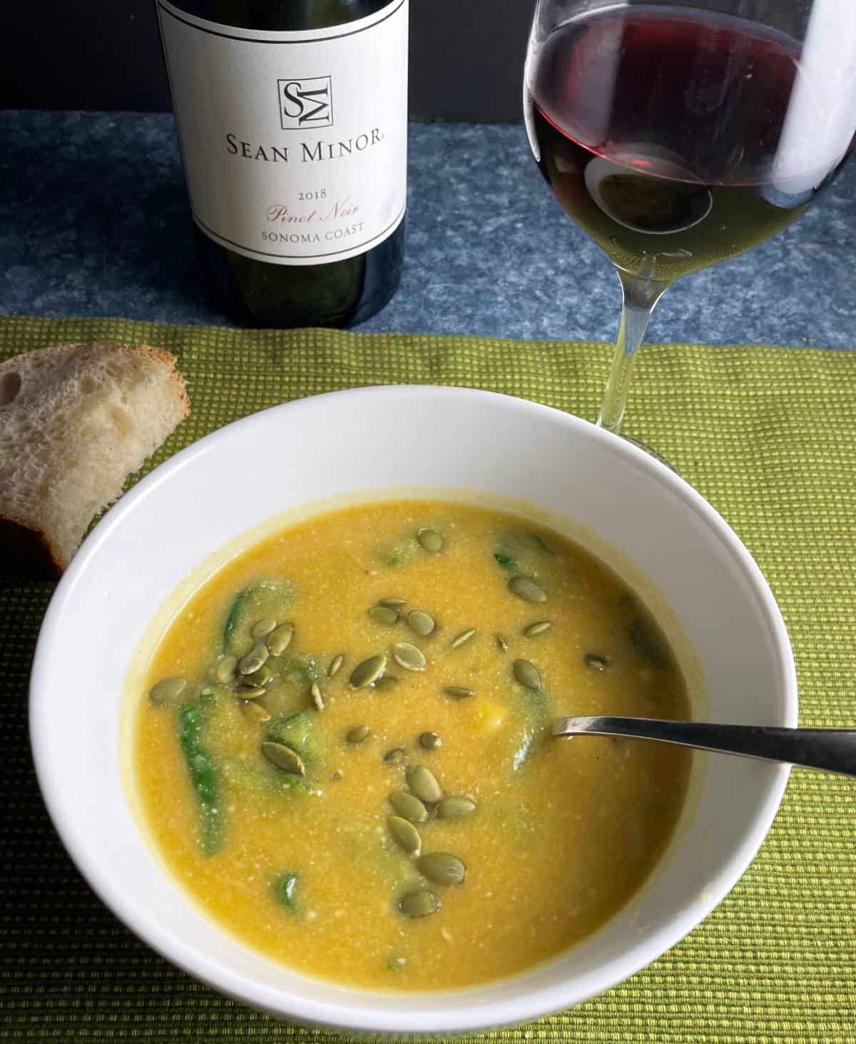 butternut squash and spinach soup in a white bowl, topped with pumpkin seeds. Served with a Pinot Noir red wine.