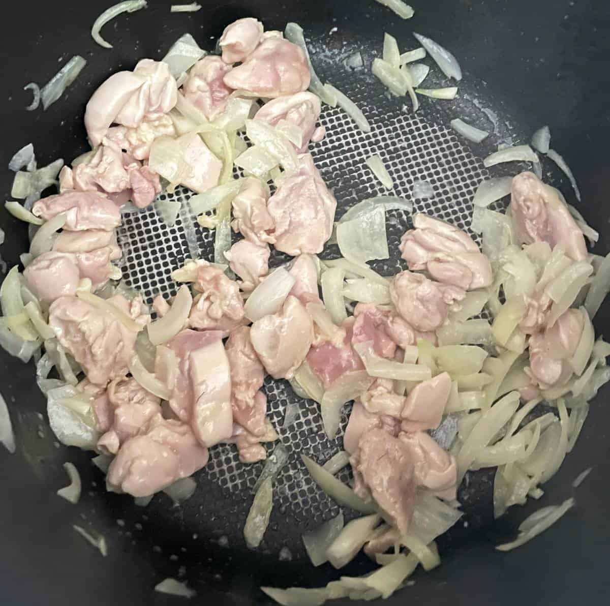 chicken starting to turn white as it cooks in a black pan along with some onions.