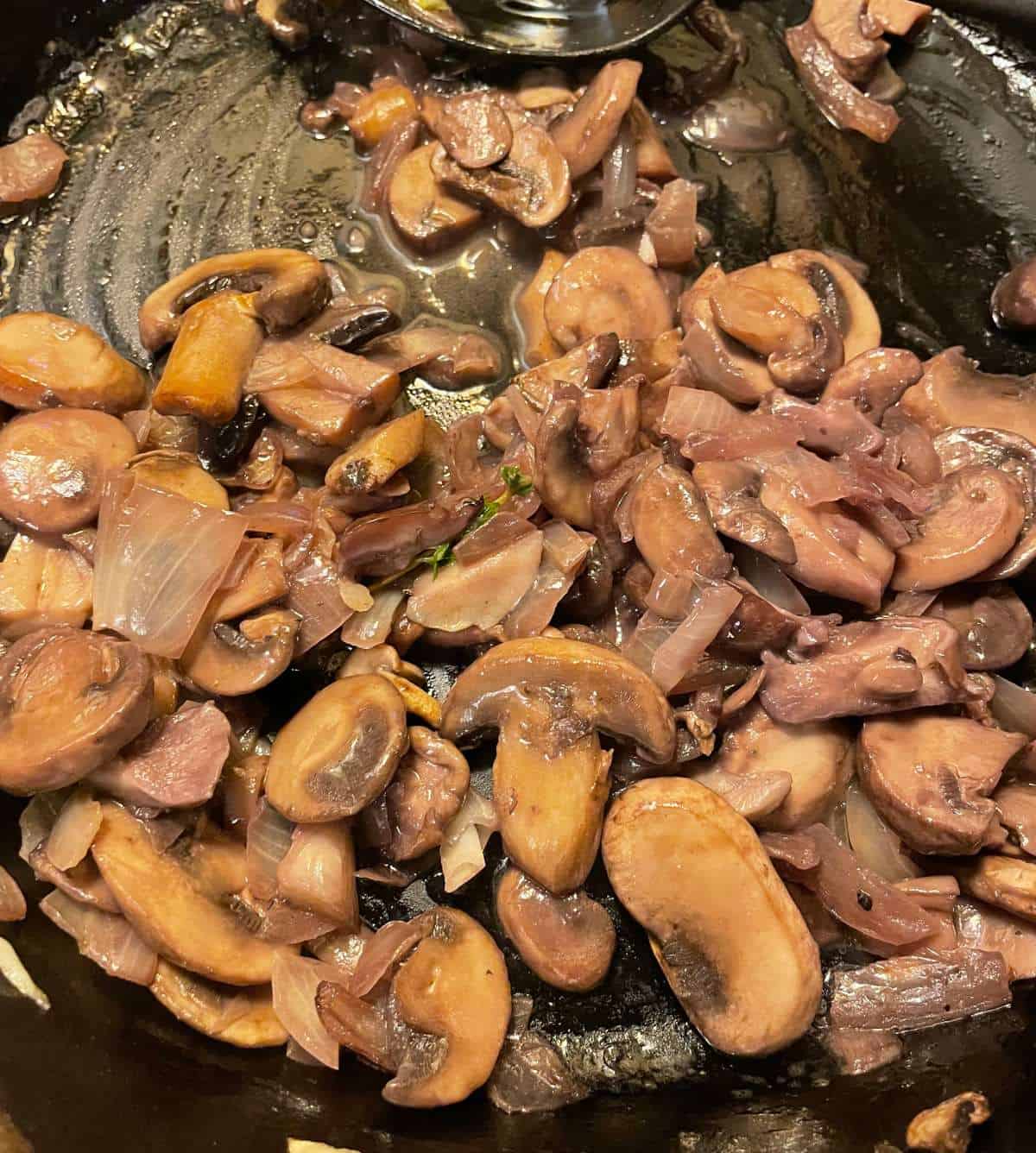 sliced mushrooms cooking in a black skillet.