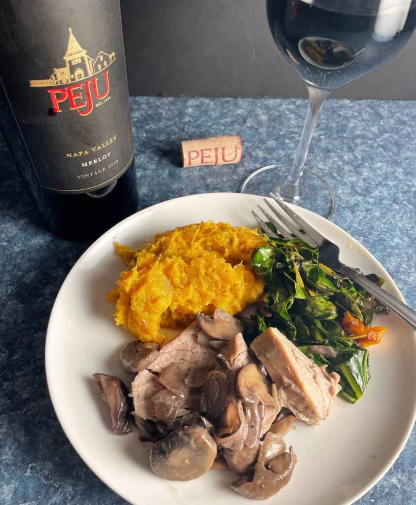 pork tenderloin with mushrooms served with sweet potatoes and greens, with a bottle of Merlot wine in the background.