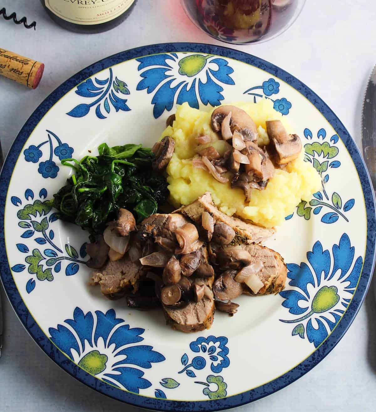 Pork tenderloin topped with mushroom sauce, served with mashed potatoes and greens.