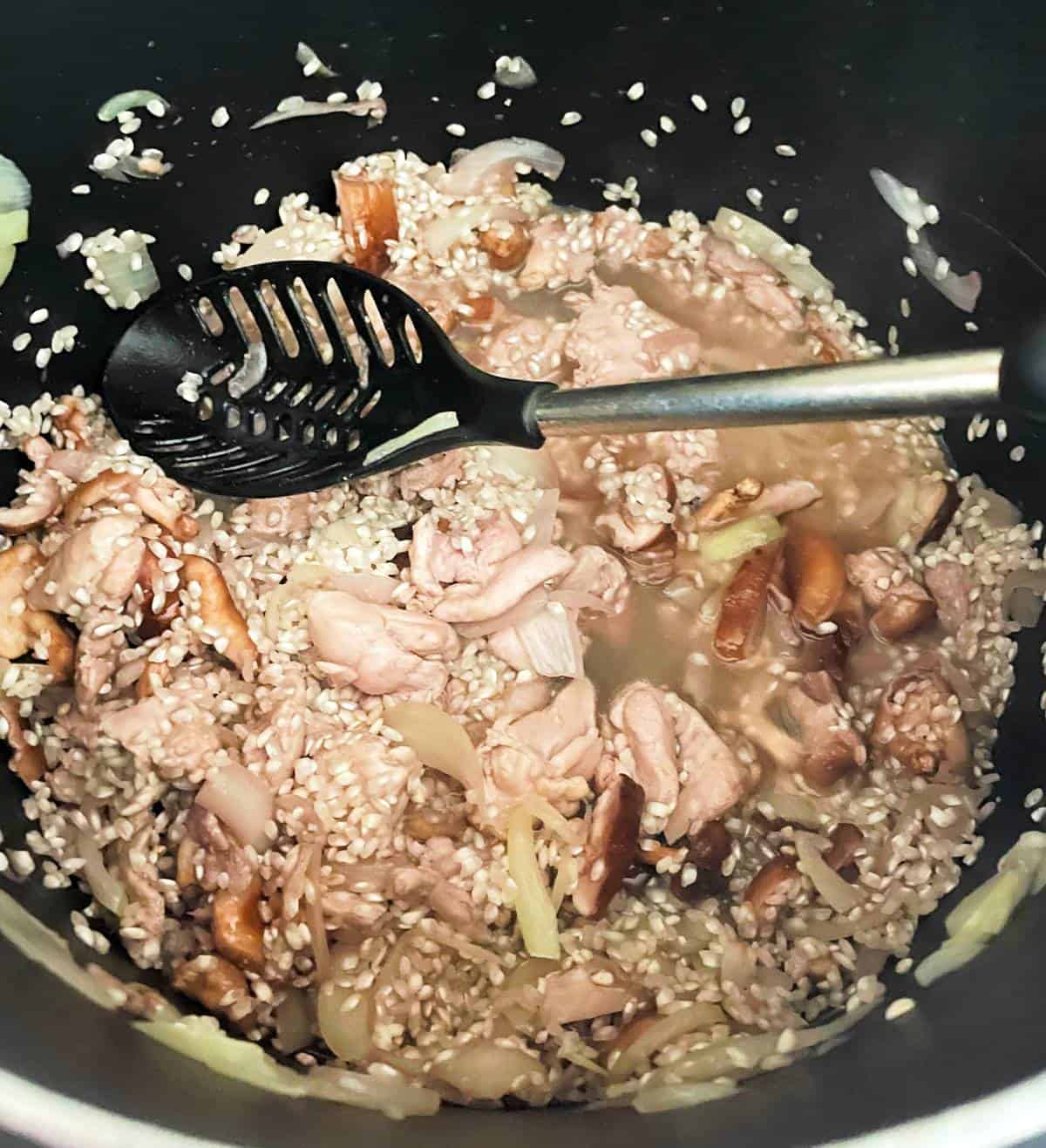 broth added to chicken and mushroom risotto in a black pot.