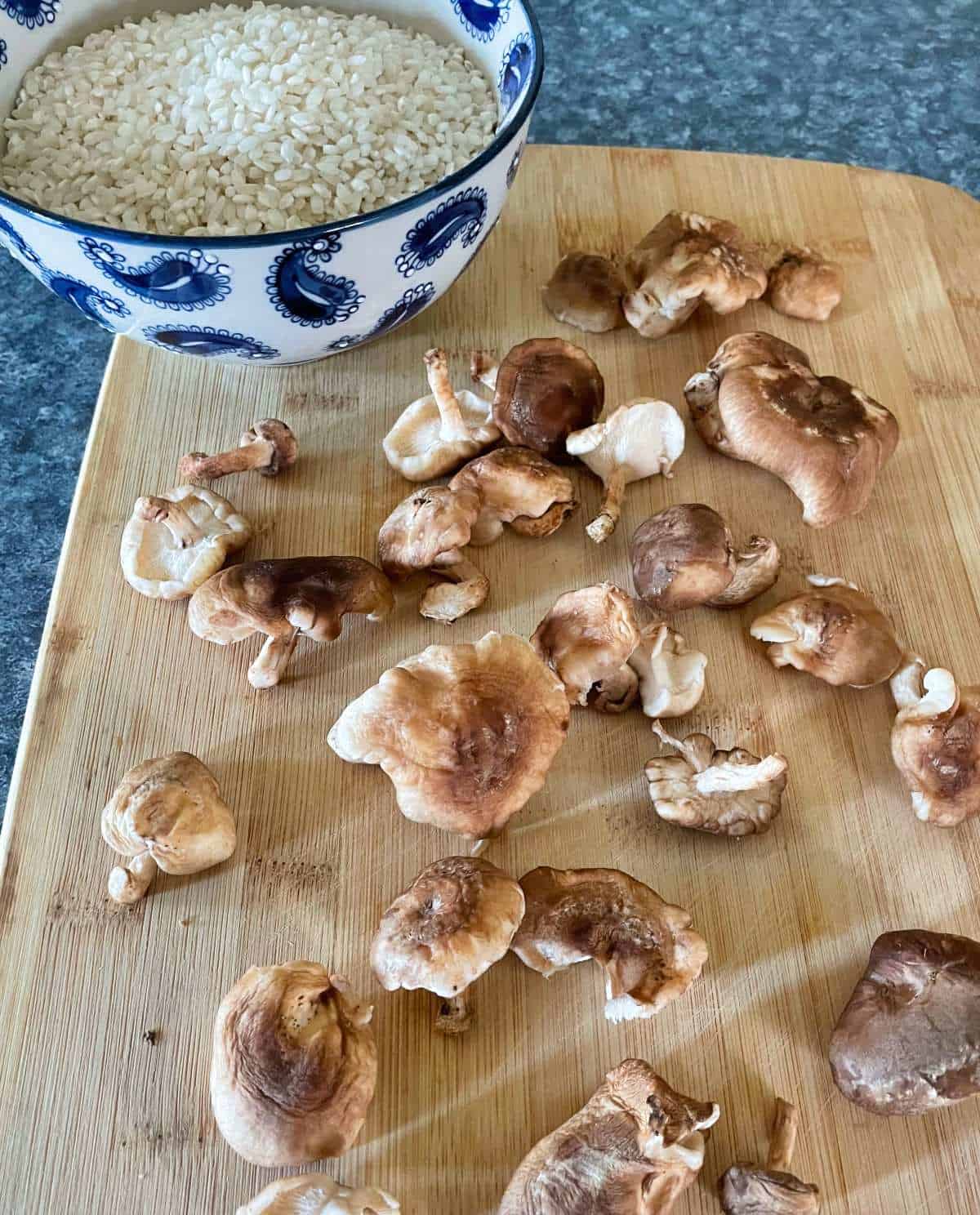 shiitake mushrooms on a cutting board with arborio rice in a bowl in the background