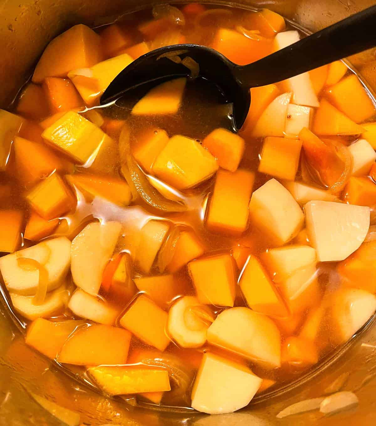 butternut squash simmering with potatoes, carrots and broth in a soup pan.