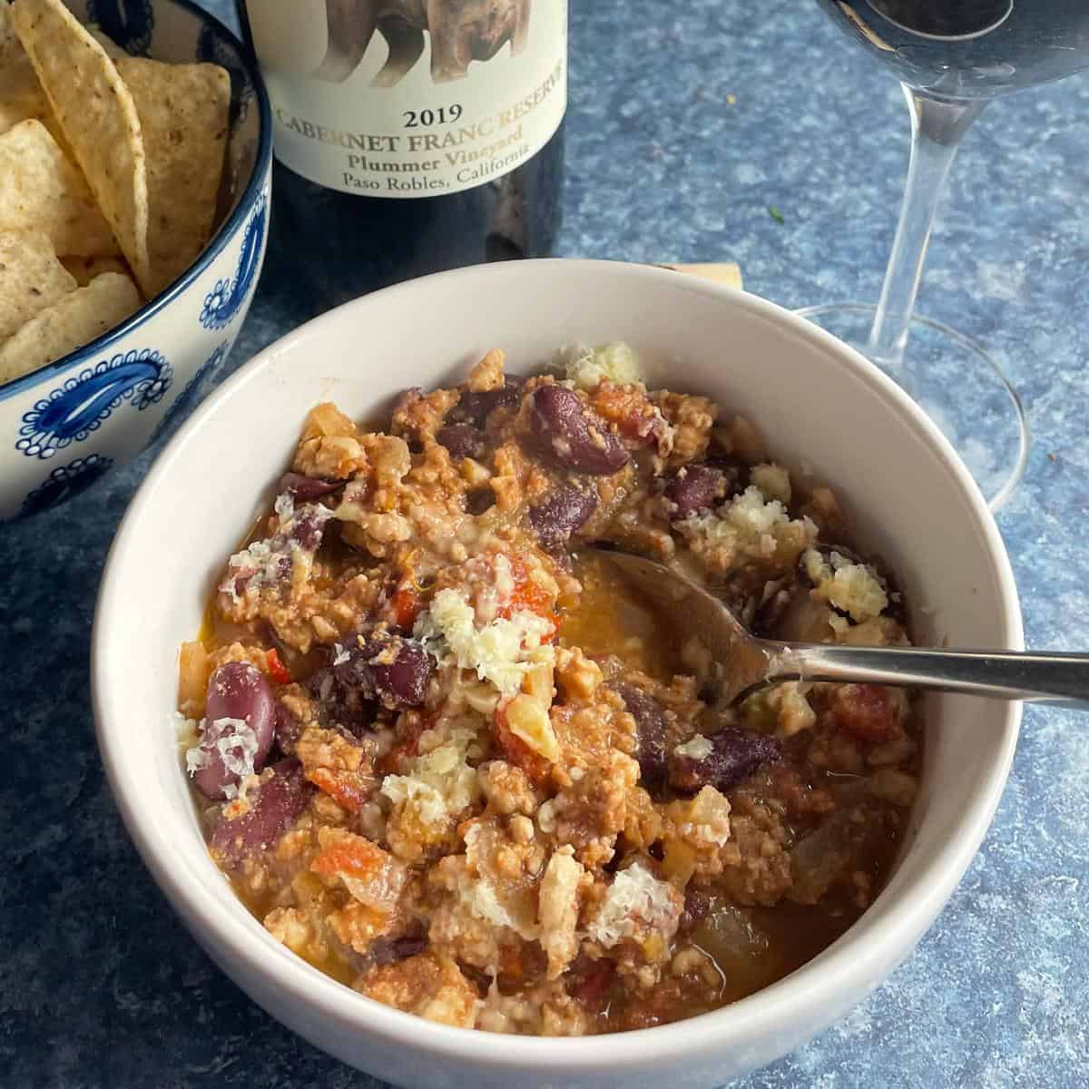 white bowl with turkey chili made with Hatch chiles, served with a red wine.