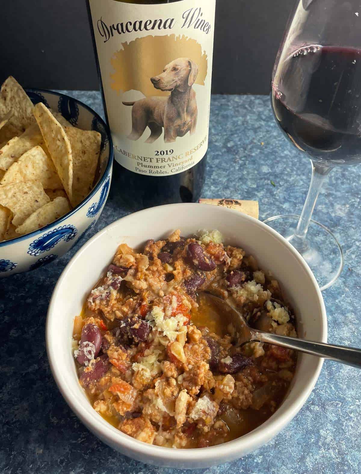 white bowl of Hatch chili with turkey, topped with cheese, and paired with a Cabernet Franc wine.