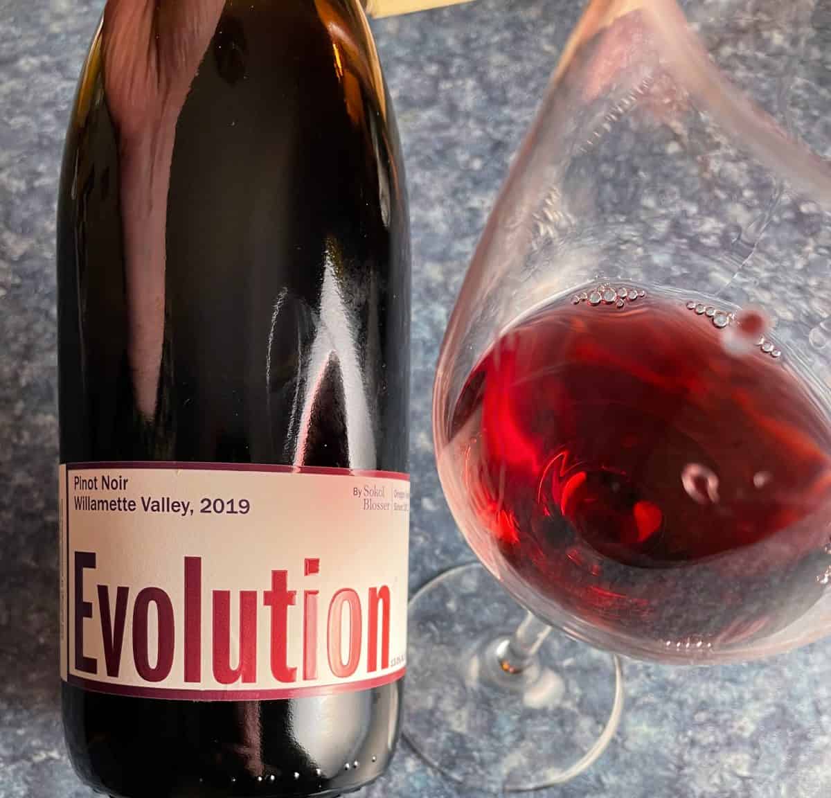 Bottle of Evolution Pinot Noir alongside a glass of this red wine. 