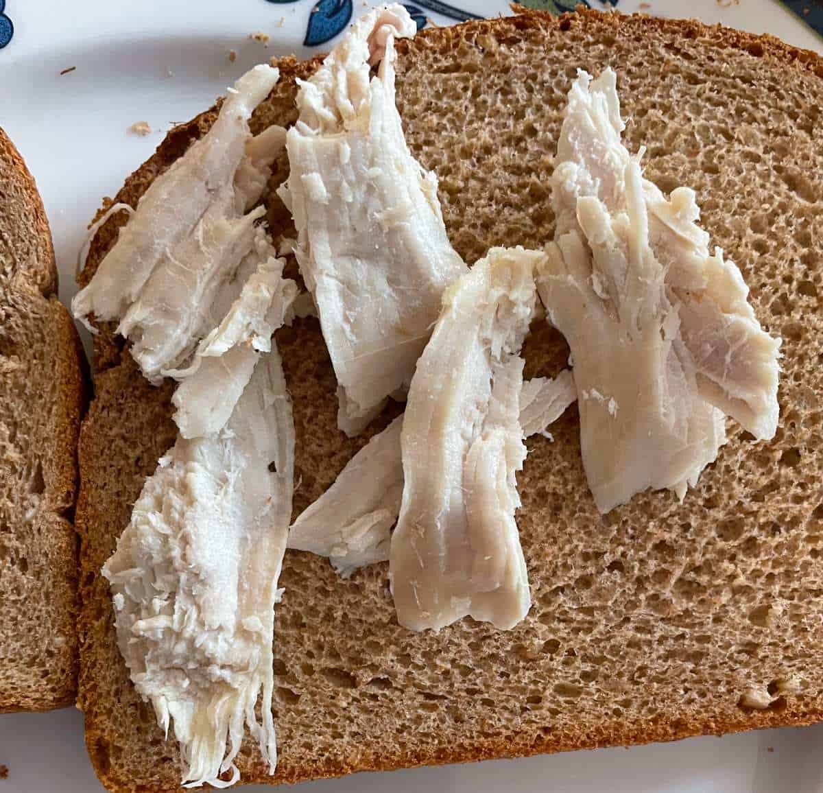 slice of wheat bread with a few pieces of leftover turkey on top of it.