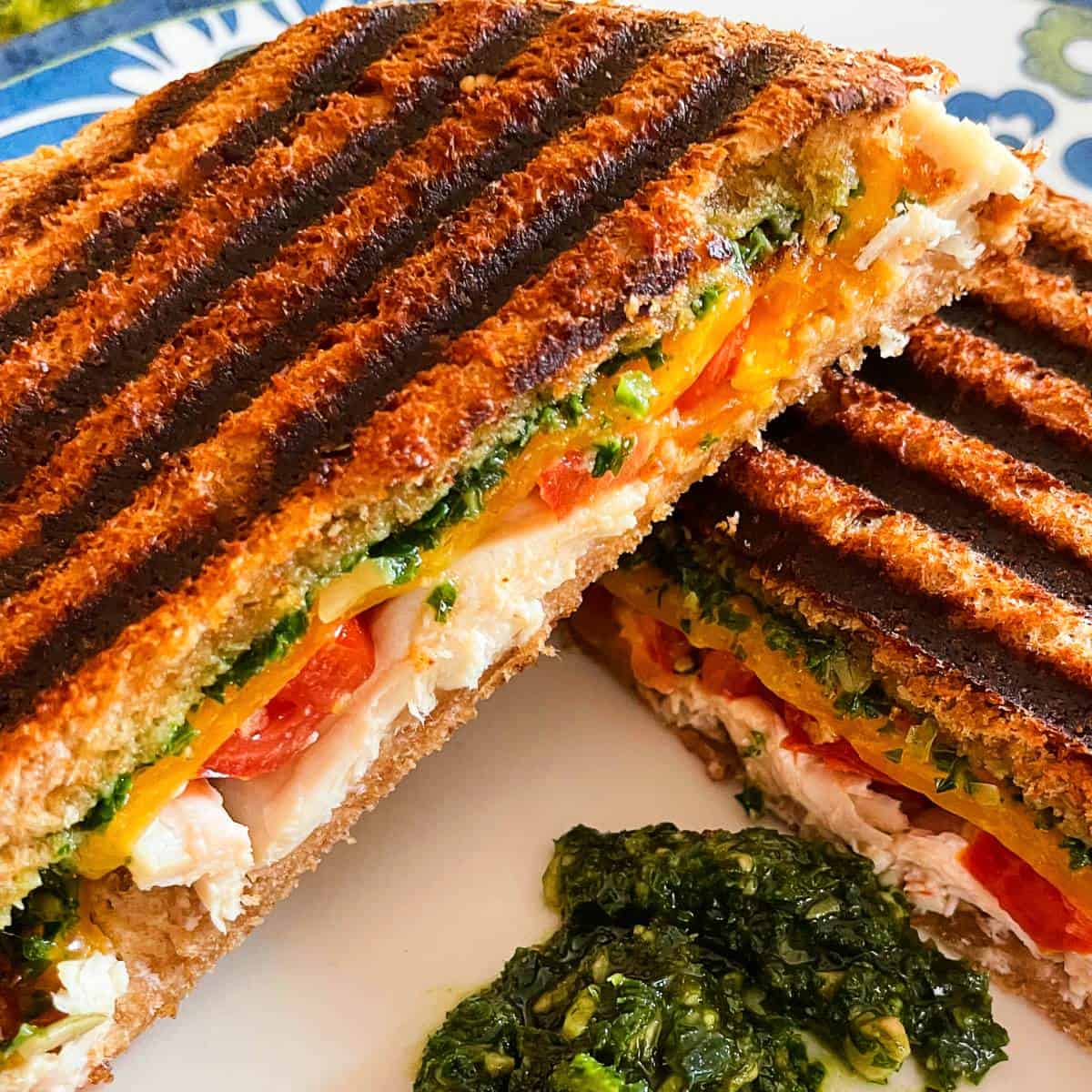 closeup photo of a turkey pesto panini sandwich served with an extra dollop of pesto sauce.
