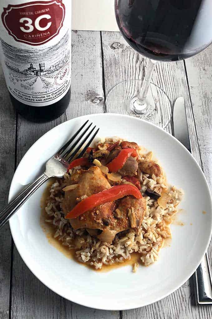 Chicken chilindron, a Spanish braised chicken dish, served over rice on a white plate. Served with a Spanish red wine. 