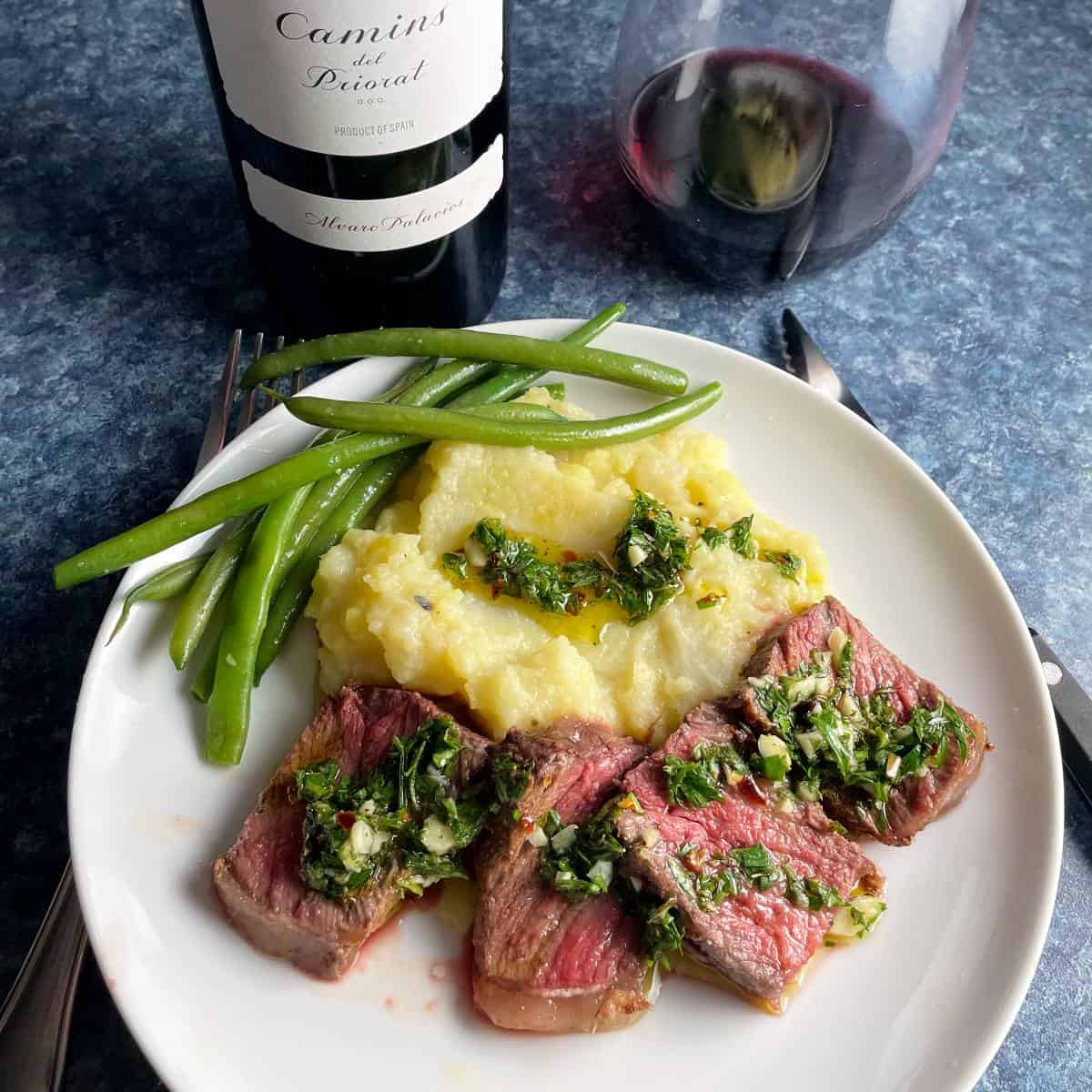 slices of medium rare steak topped with carrot top chimichurri, served with mashed potatoes, green beans and red wine.