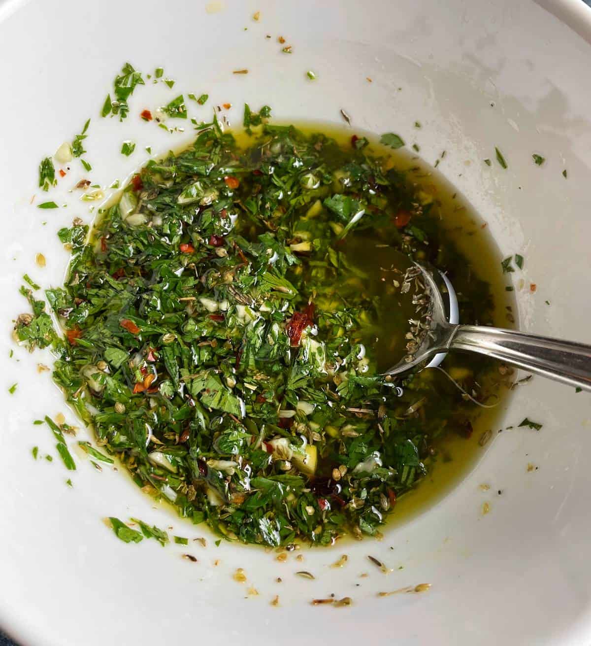 carrot top chimichurri in a while bowl, with a tablespoon dipping into the sauce.