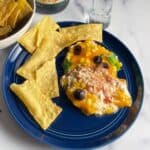 fiesta dip, made with cheese, sour cream, beans and more, on a blue plate with tortilla chips.