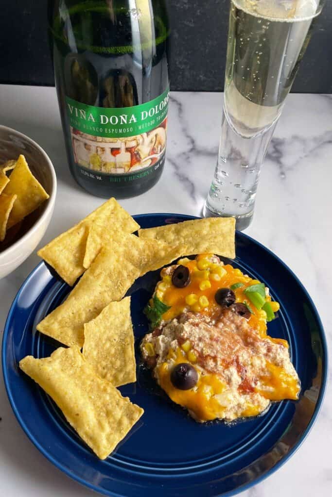 fiesta dip served with tortilla chips on a plate, along with sparkling wine.