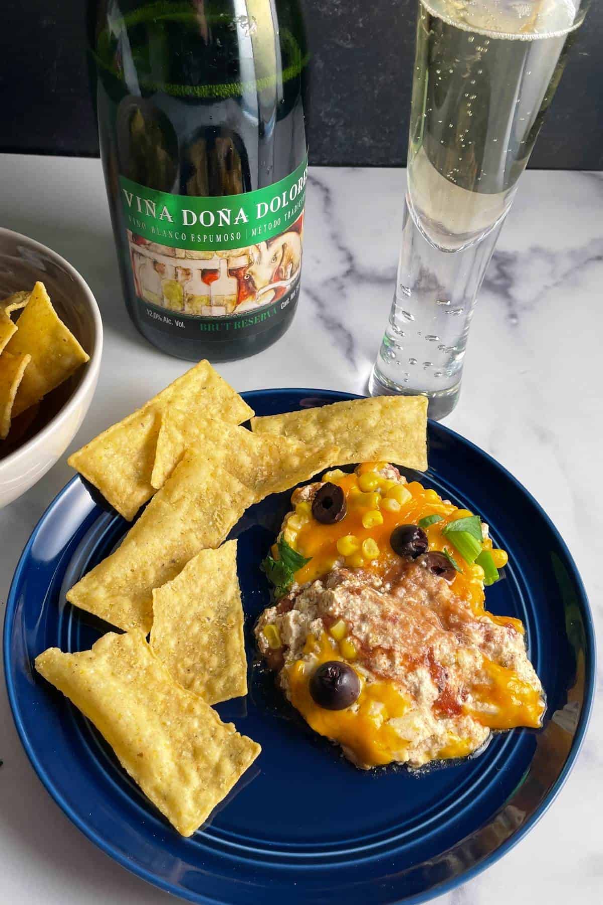 Fiesta dip on a blue plate with tortilla chips, served with a Mexican sparkling wine.