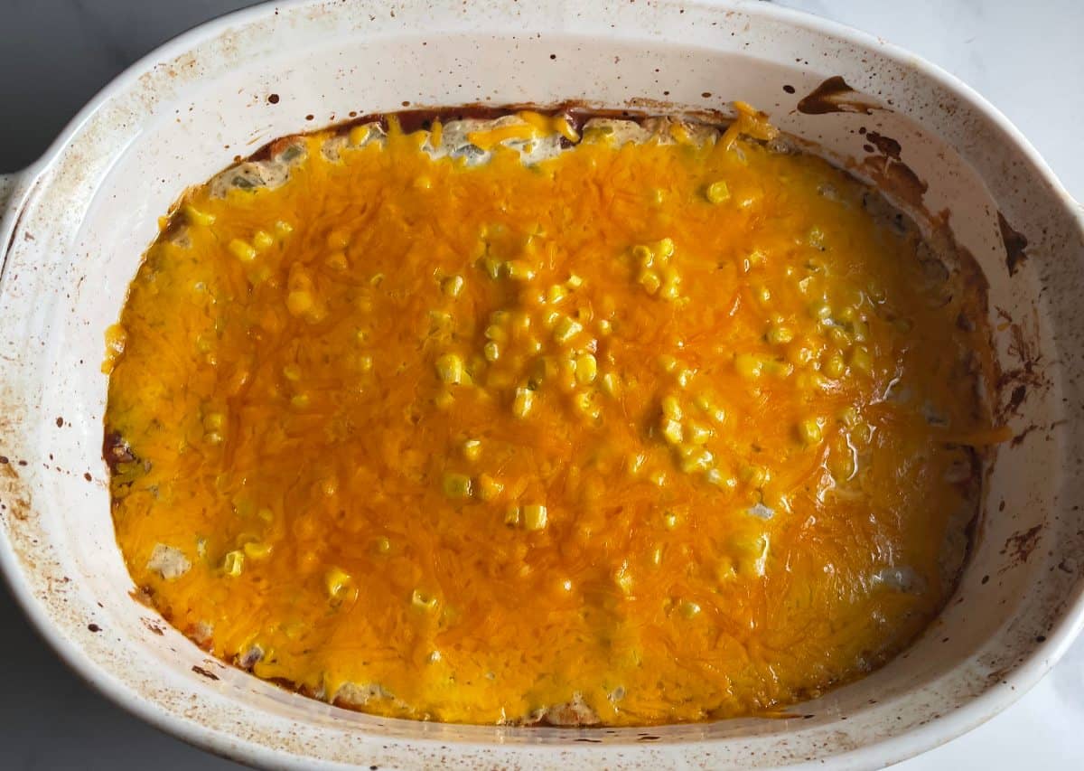 Fiesta dip in a white baking dish, just removed from the oven. Shown from above, with a layer of melted cheese on top.