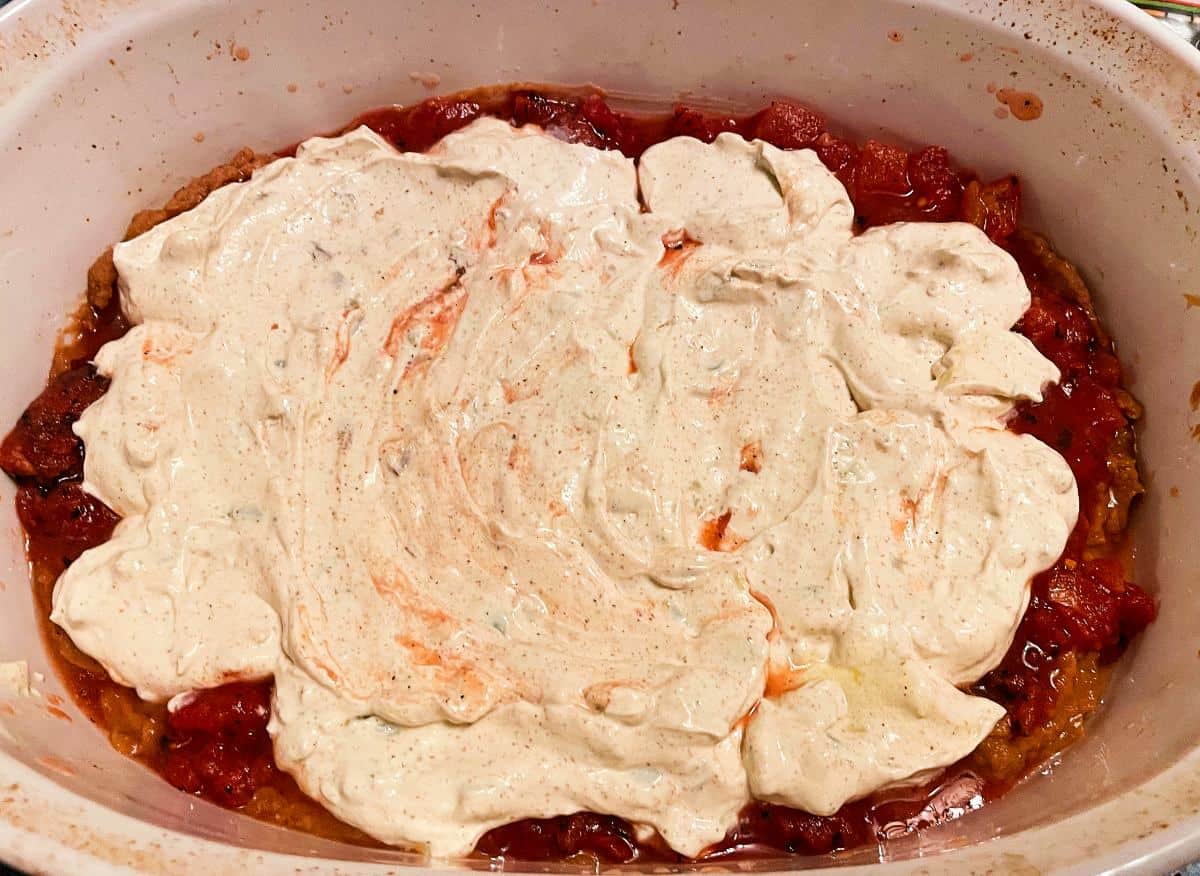 sour cream with spices spread over tomatoes in a baking dish, to make fiesta dip.