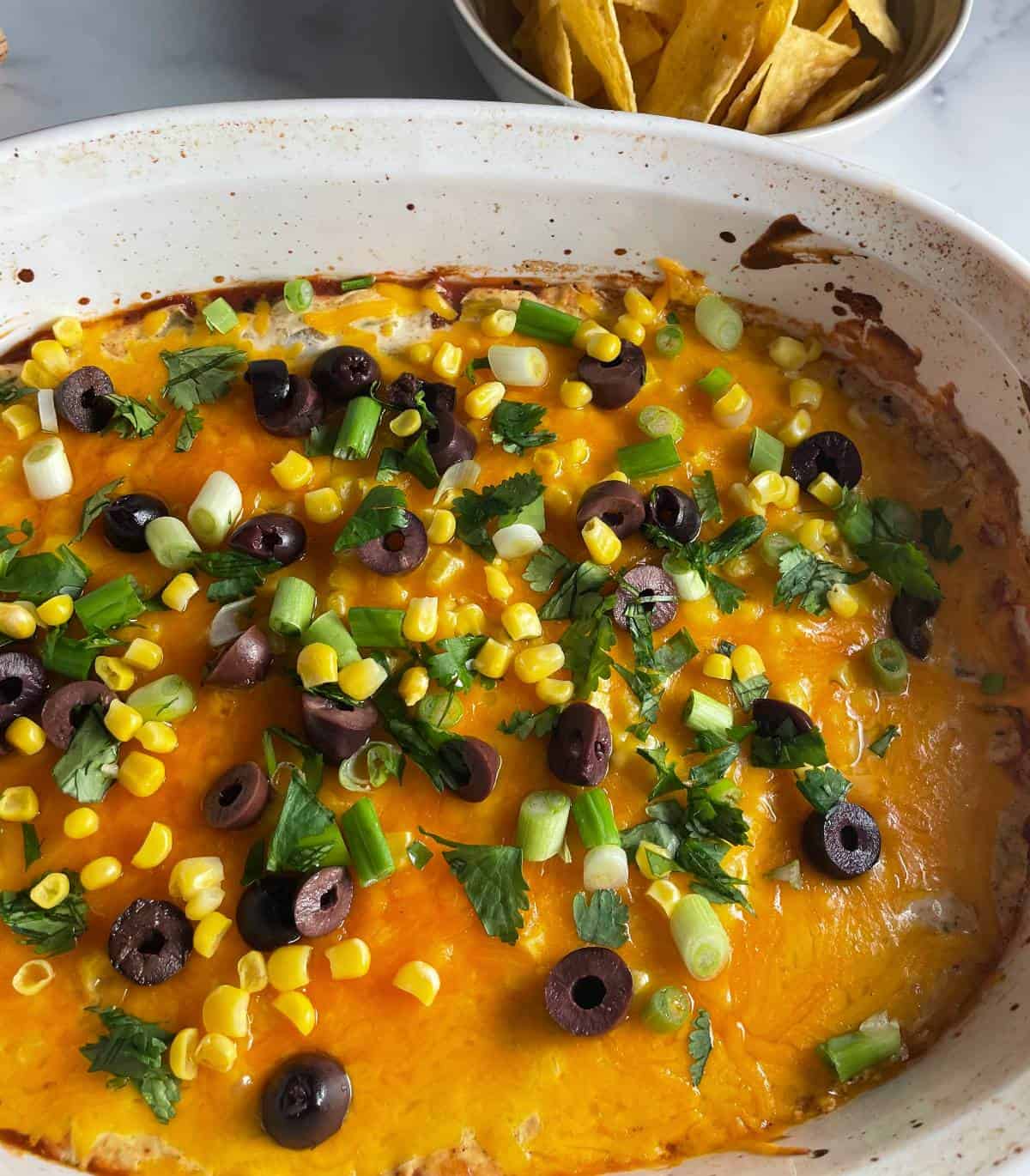 baked fiesta dip with corn, scallions cilantro and olives on top.