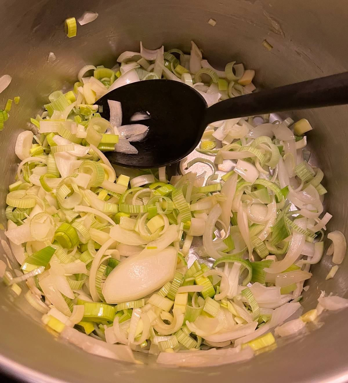 stirring leeks and onions in a silver soup pot.