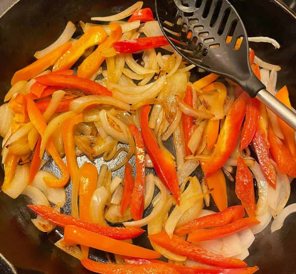 peppers and onions cooking in a black skillet.