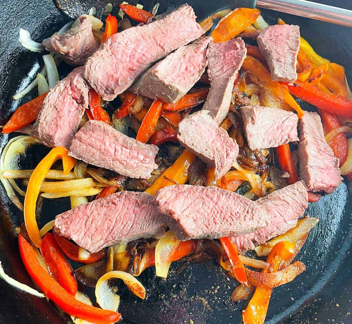 slices of leftover steak in a black cast iron skillet with onions and peppers.