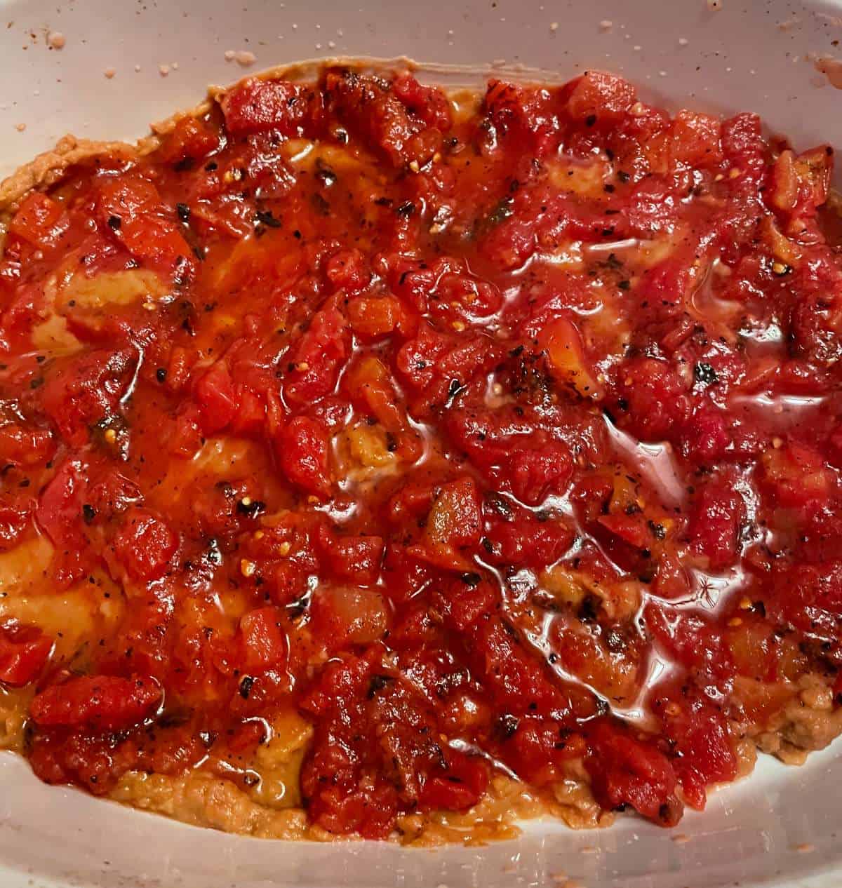 layer of diced tomatoes covering refried beans in a baking dish.