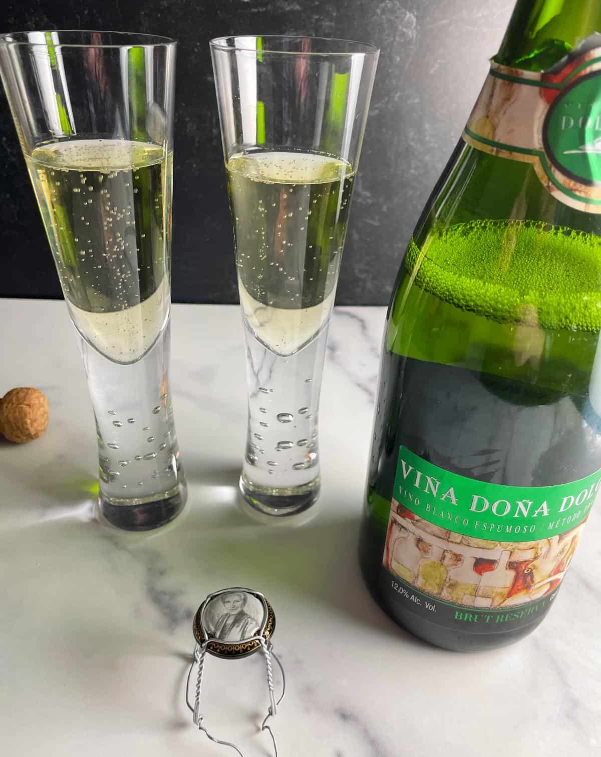 Two flutes with sparkling wine, alongside a bottle of Vina Dona Dolores bubbly.