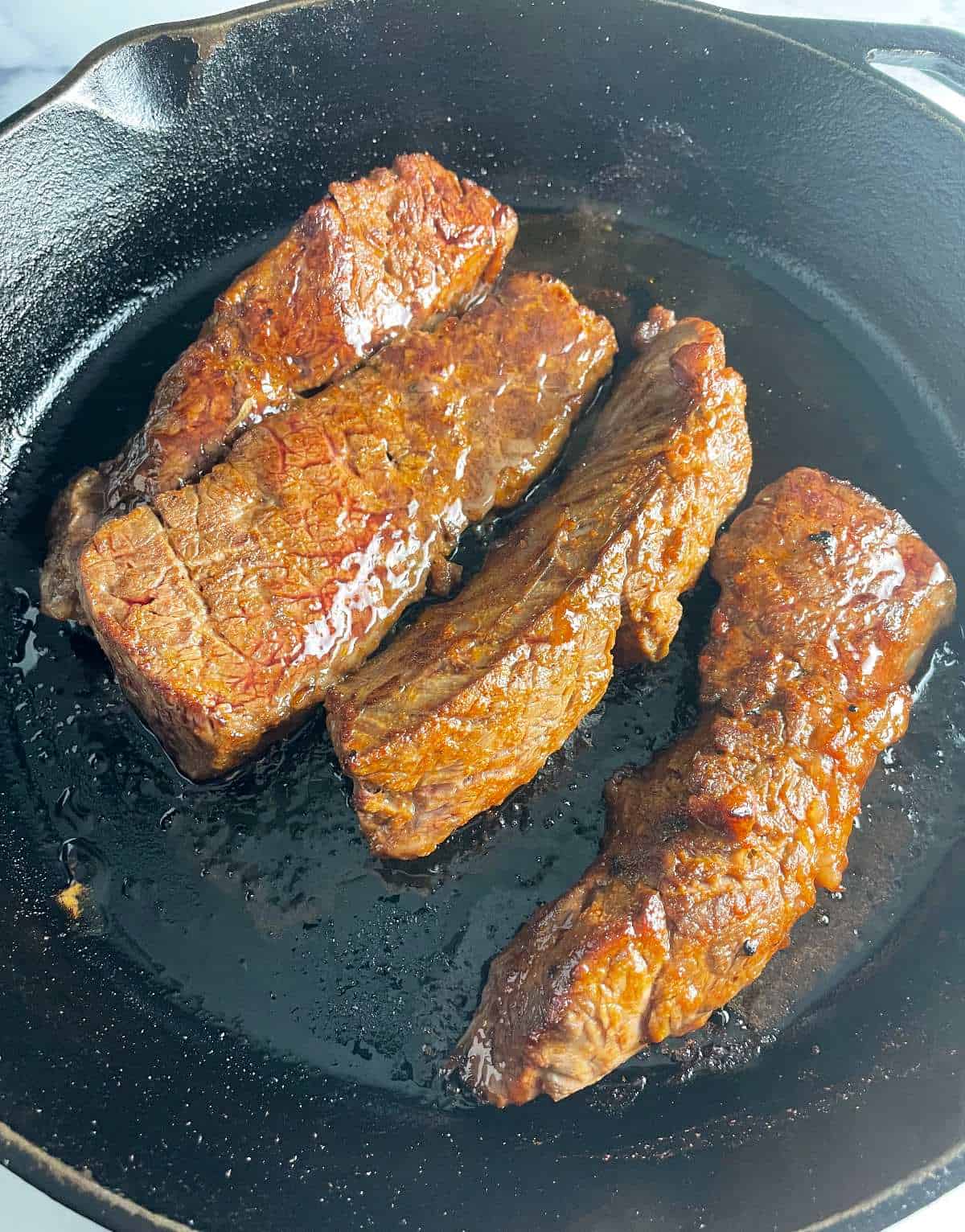 Oven baked steak tips in a black skillet.