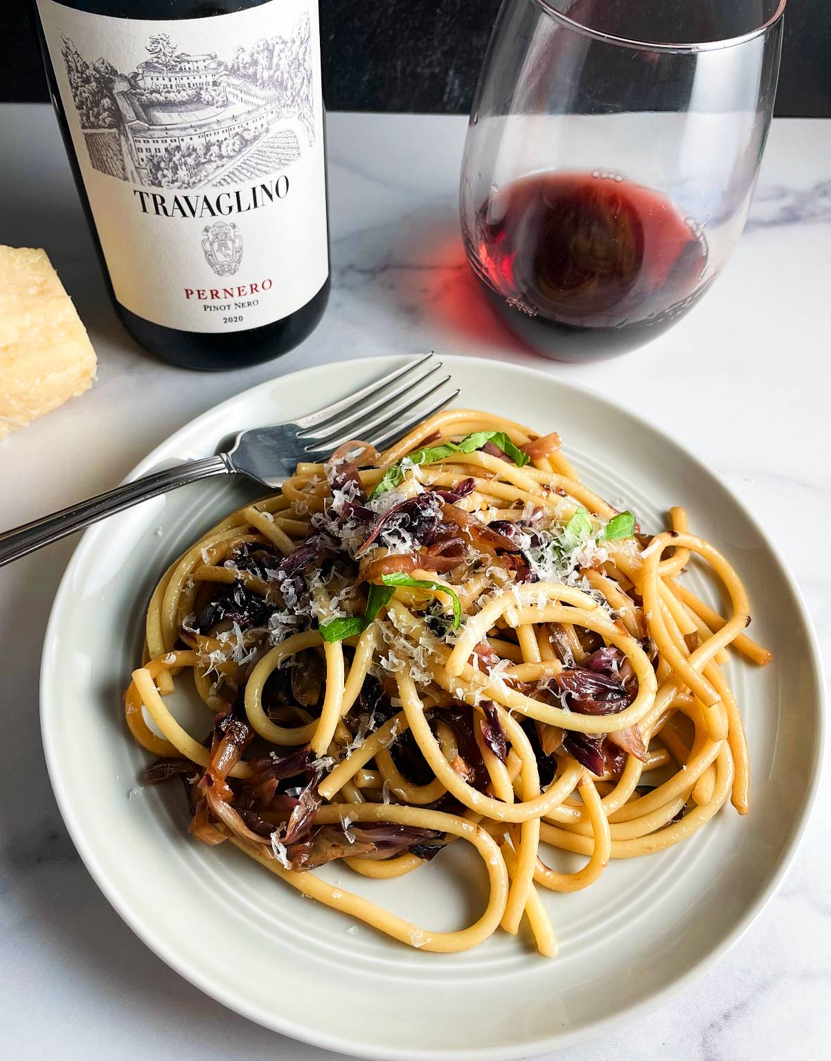plate with bucatini pasta tossed with sautéed radicchio. Served with a red wine.