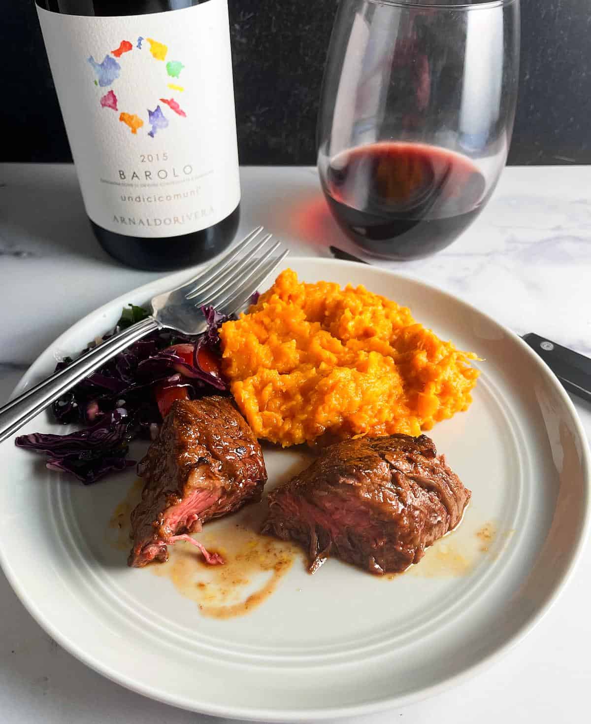 steak tips plated with sweet potatoes and red cabbage salad, with a red wine in the background.