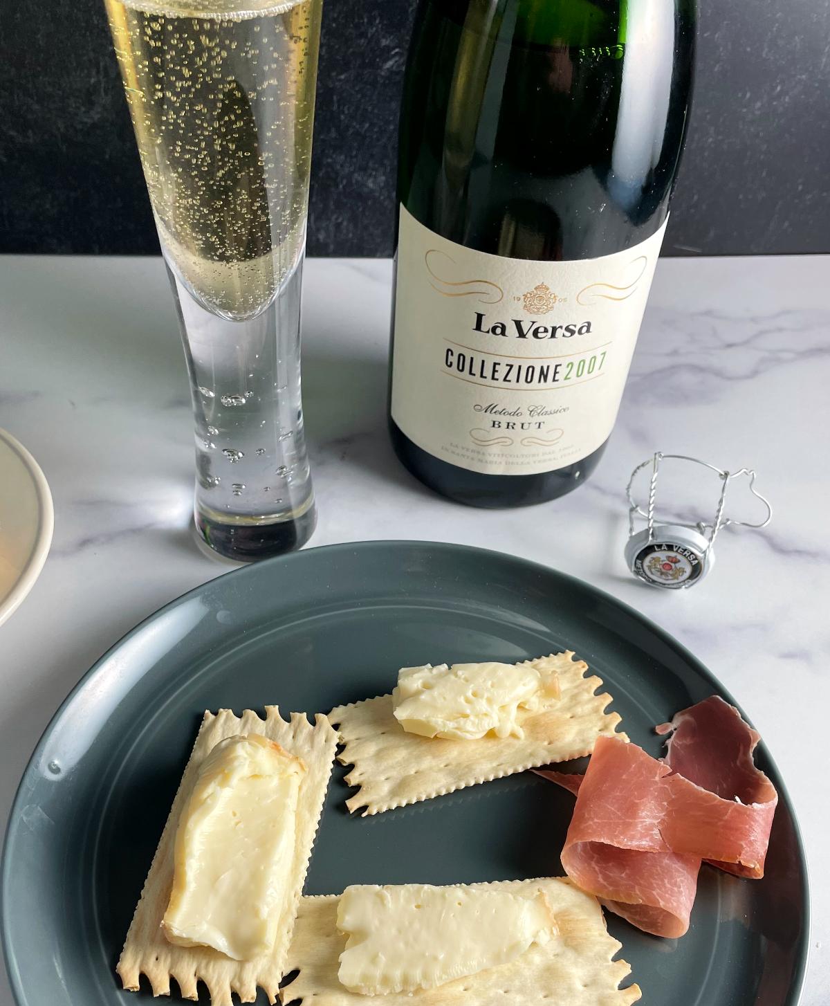 plate with taleggio cheese spread over crackers, along with some prosciutto. Pairing with sparkling wine from Oltrepo Pavese.