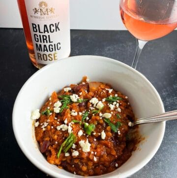 Spicy lentil chili in a white bowl served with rosé wine