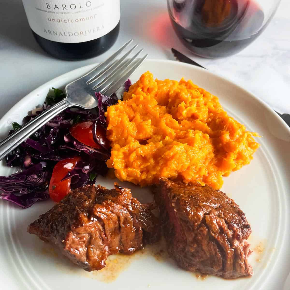 oven baked steak tips on a grey plate with mashed sweet potatoes and red cabbage.